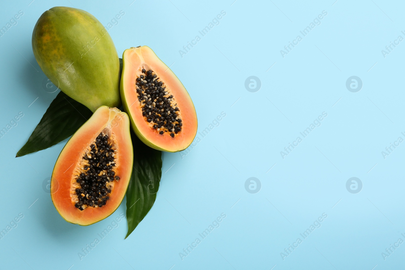 Photo of Fresh ripe papaya fruits with green leaves on light blue background, flat lay. Space for text