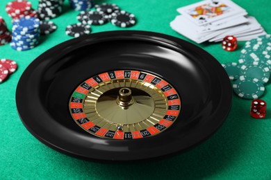 Photo of Roulette wheel, playing cards, chips and dice on green table, closeup. Casino game