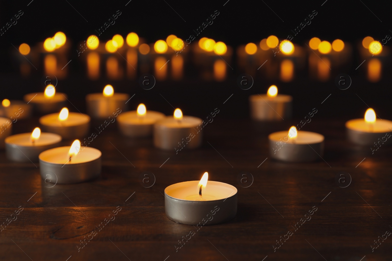 Photo of Wax candles burning on table in darkness, closeup