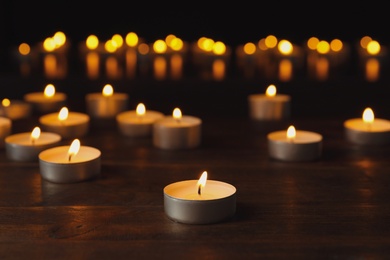 Photo of Wax candles burning on table in darkness, closeup