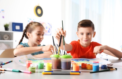 Photo of Little children painting picture at table indoors