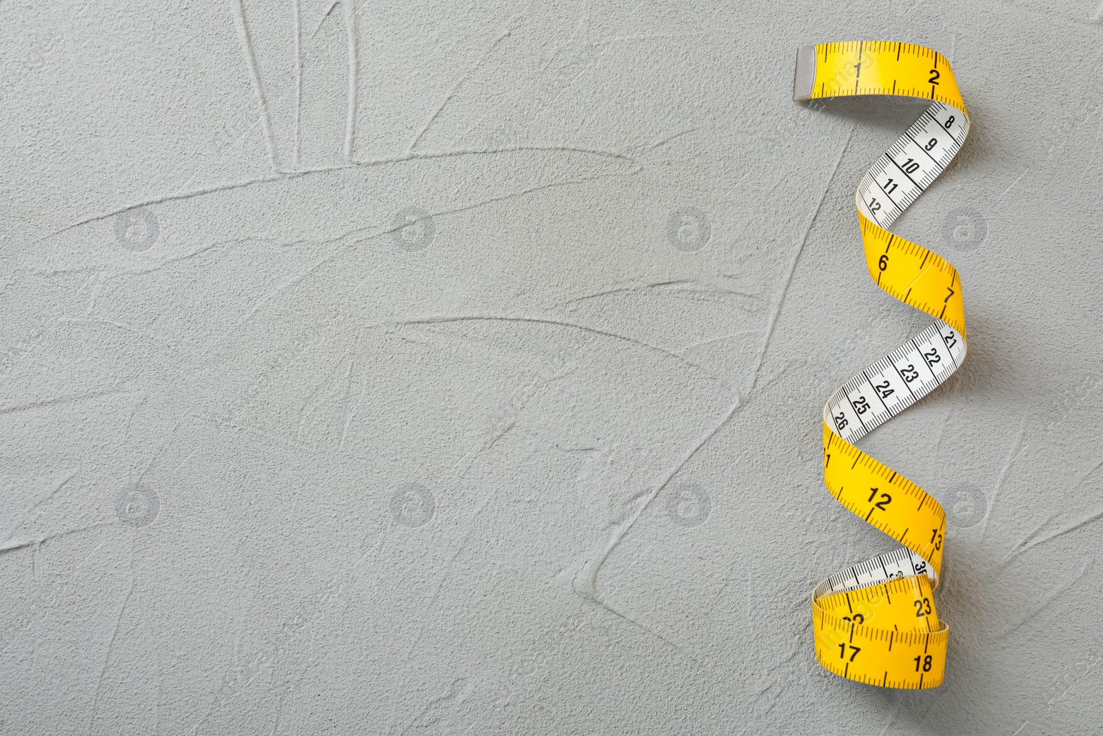 Photo of Yellow measuring tape on light grey stone table, top view. Space for text