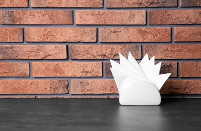 Napkin holder with paper serviettes on table against brick wall. Space for text