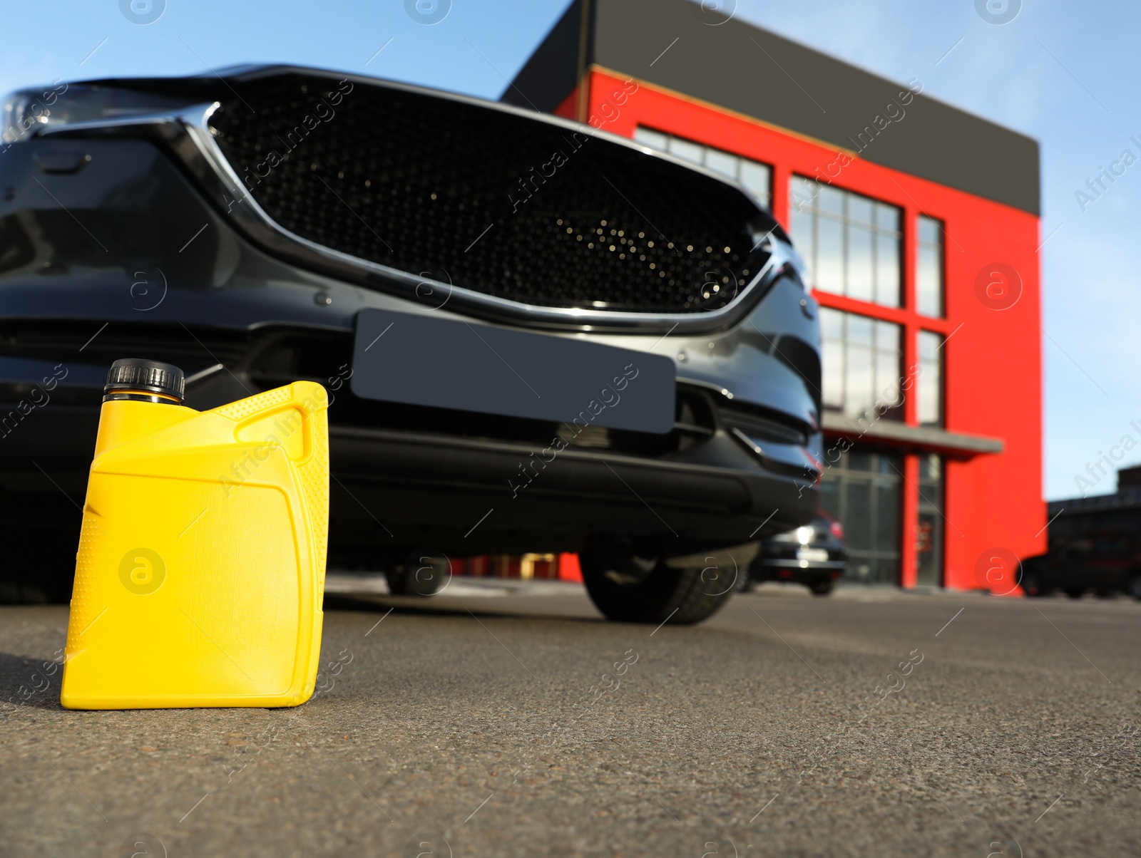 Photo of Yellow canister with motor oil near car on asphalt road, low angle view