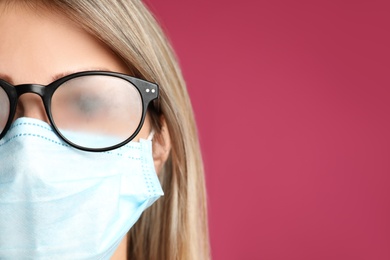 Photo of Woman with foggy glasses caused by wearing disposable mask on pink background, space for text. Protective measure during coronavirus pandemic