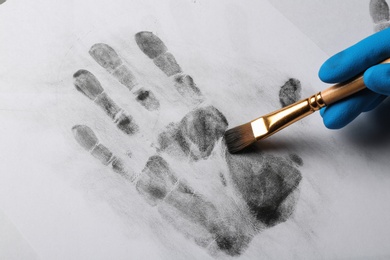 Detective taking fingerprints with brush from paper, closeup. Criminal investigation