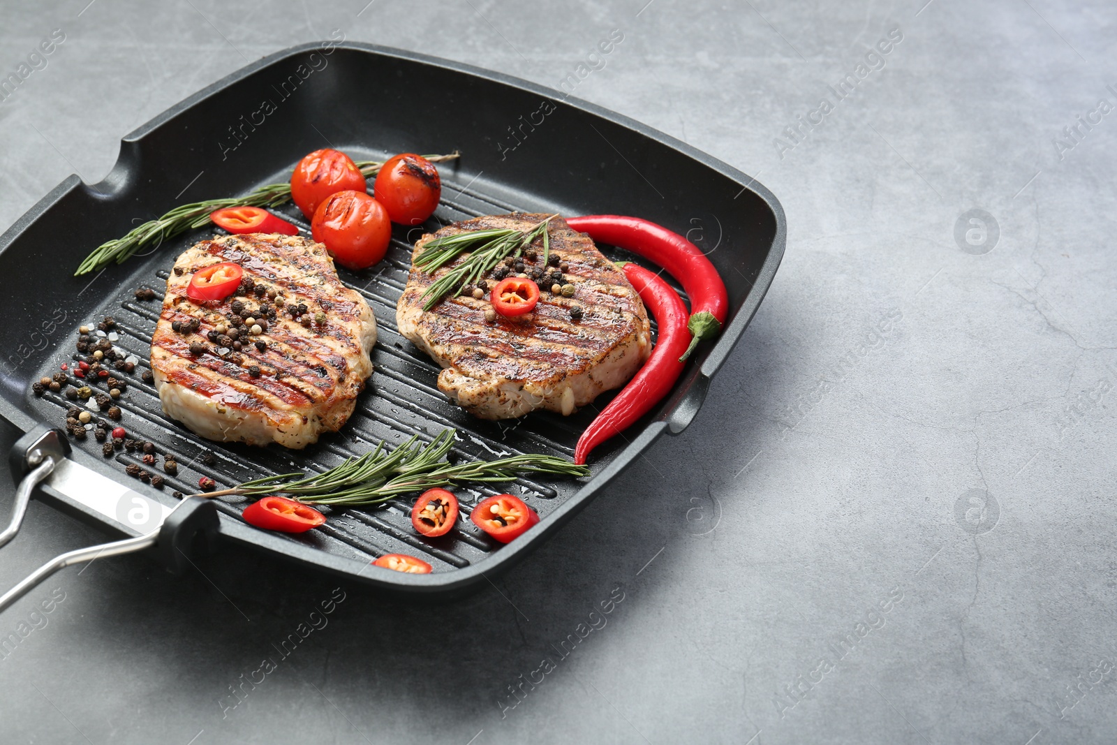 Photo of Grill pan with delicious pork steaks, spices and vegetables on grey table, space for text