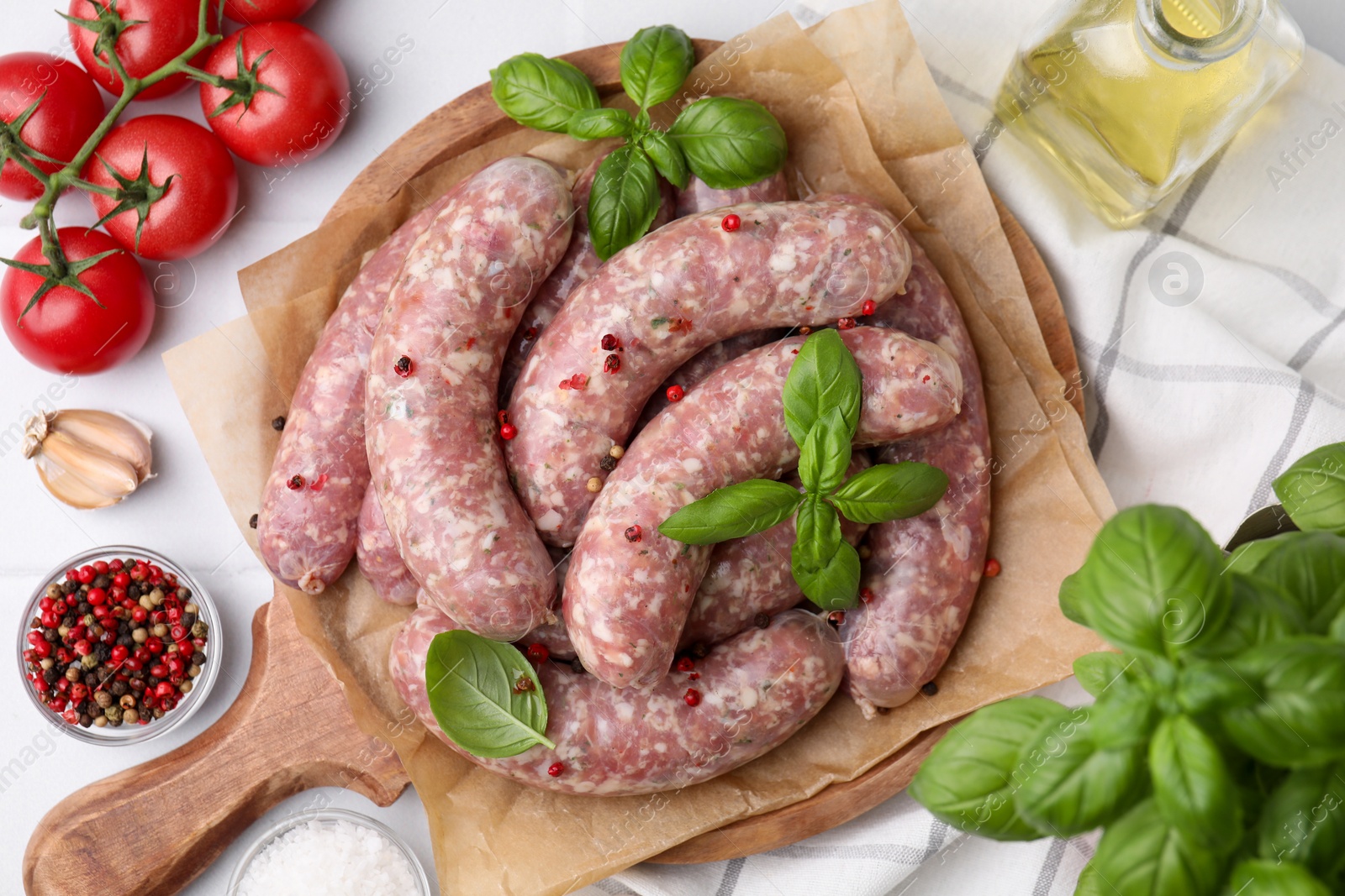 Photo of Raw homemade sausages, basil leaves, tomatoes and spices on white table, flat lay