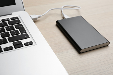 Charging modern laptop with power bank on wooden table, closeup