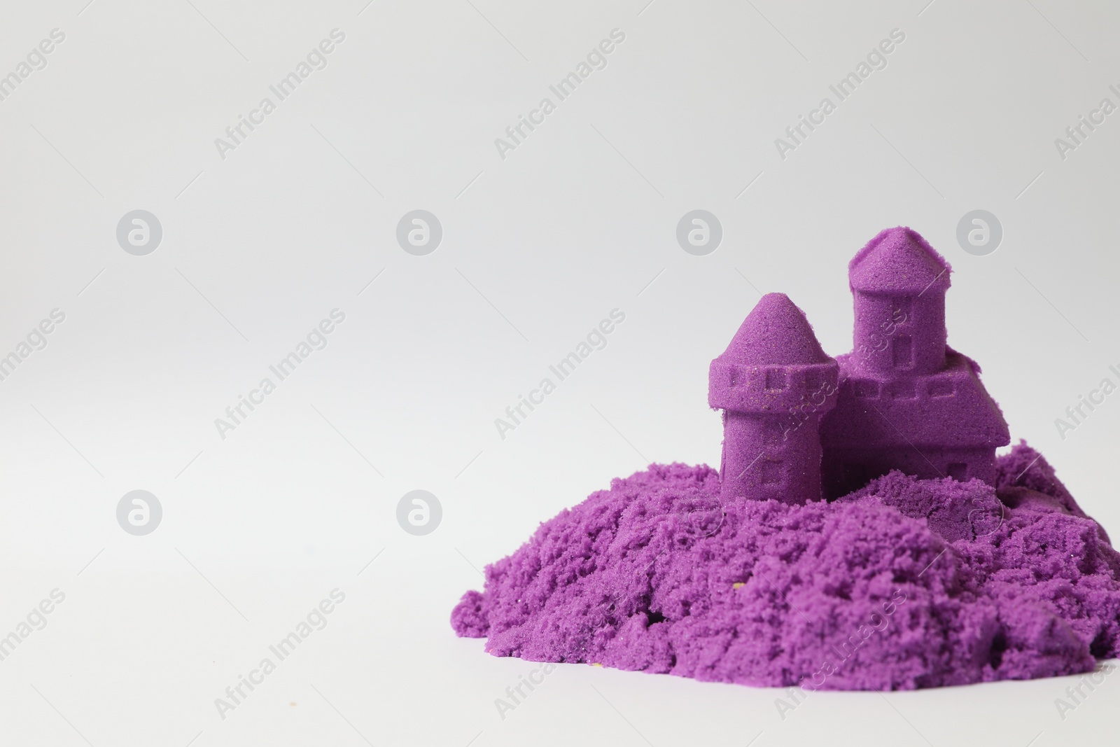 Photo of Castle made of purple kinetic sand on white background. Space for text