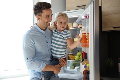Father and daughter taking bottle with juice out of refrigerator in kitchen
