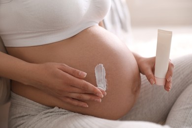 Young pregnant woman with cosmetic product indoors, closeup