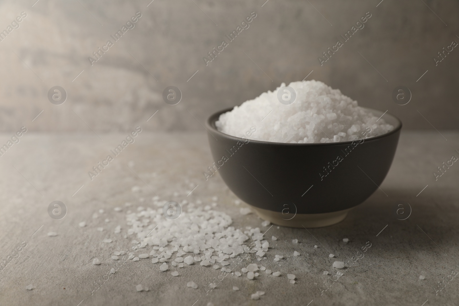 Photo of Natural salt in bowl on grey textured table, space for text