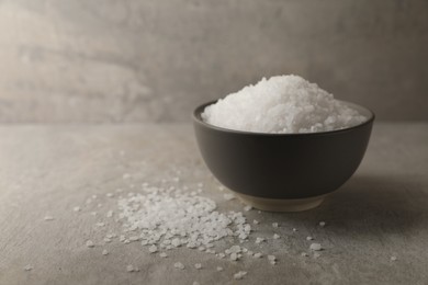 Photo of Natural salt in bowl on grey textured table, space for text