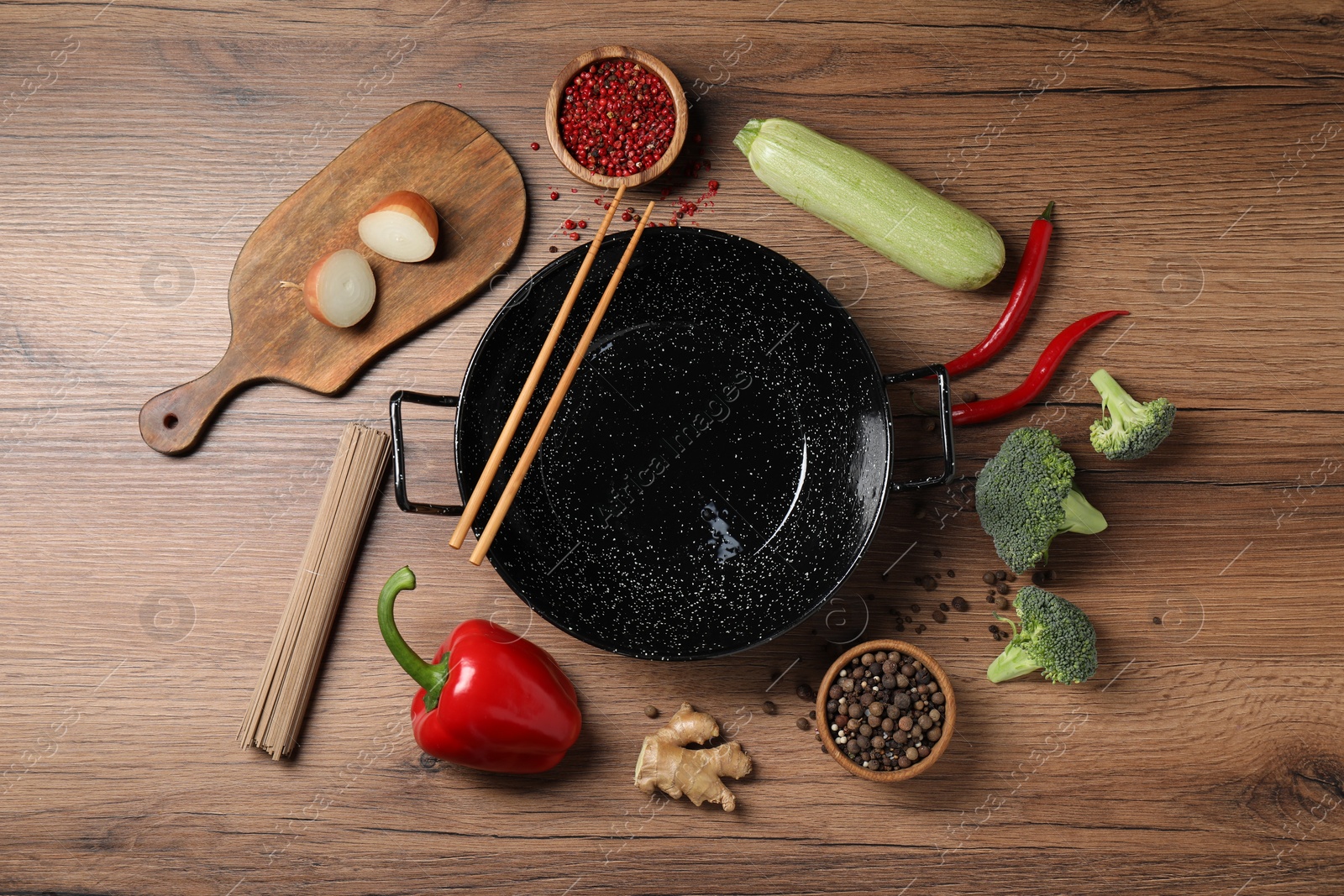 Photo of Empty iron wok surrounded by raw ingredients on wooden table, flat lay