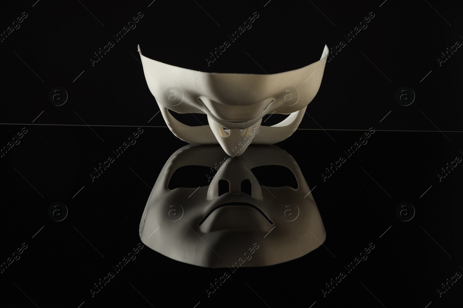 Photo of Plastic face mask on black mirror surface. Theatrical performance