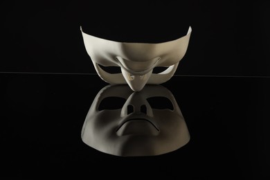 Plastic face mask on black mirror surface. Theatrical performance