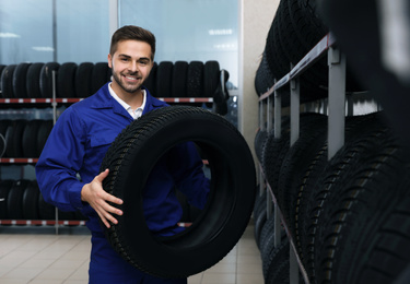 Male mechanic with car tire in auto store