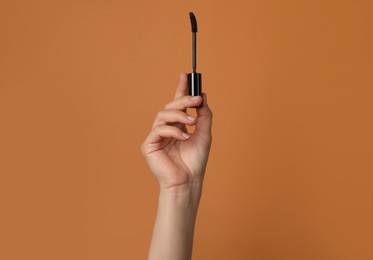 Photo of Woman holding mascara on light brown background, closeup. Space for text