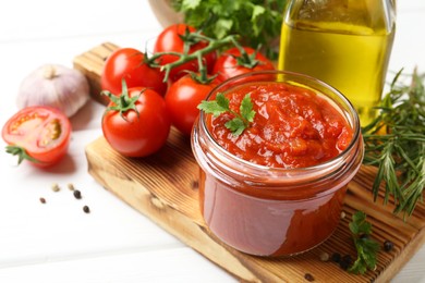 Photo of Homemade tomato sauce in jar and fresh ingredients on white wooden table, closeup