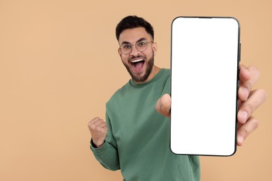 Image of Happy man holding smartphone with empty screen on beige background, space for text