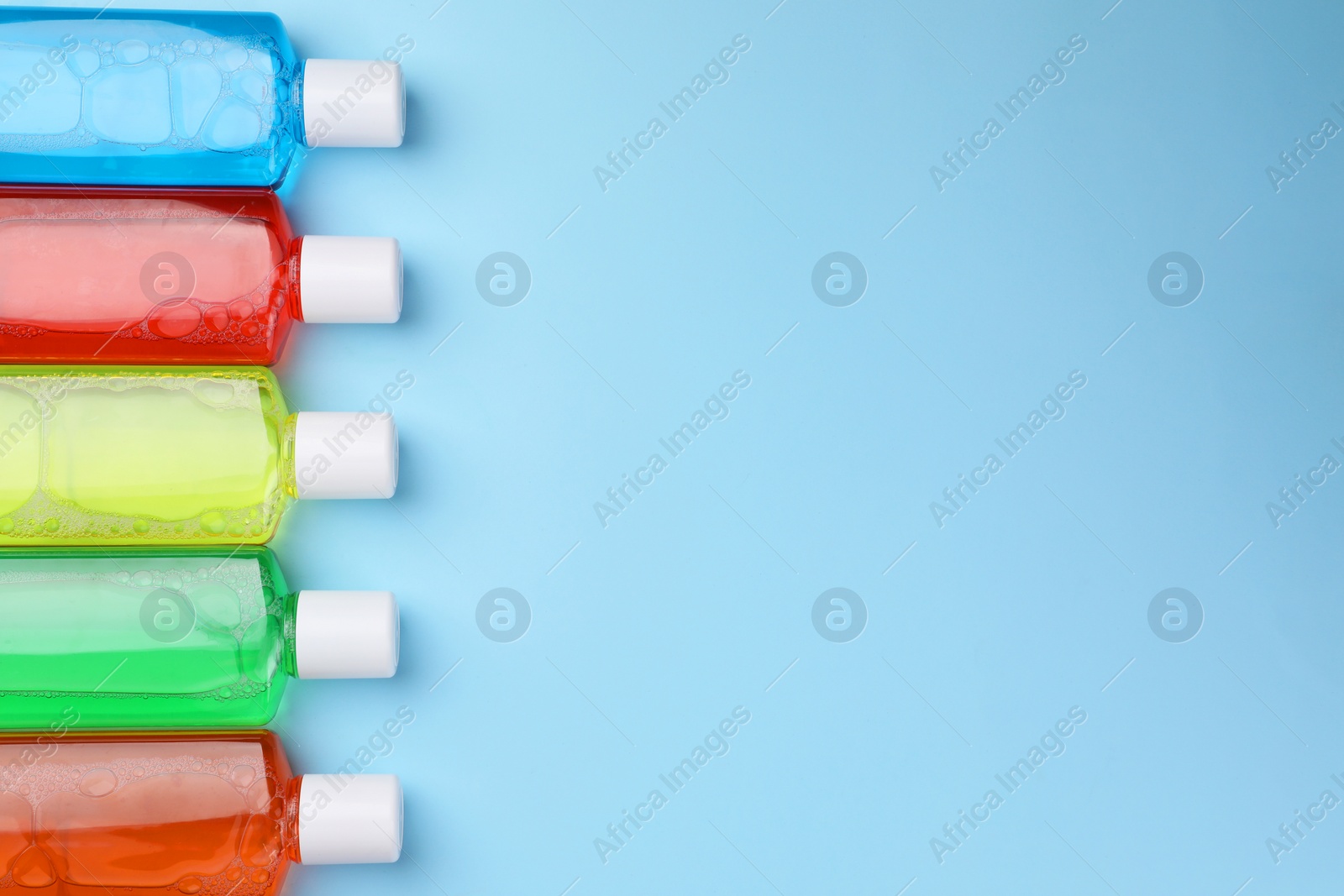 Photo of Fresh mouthwashes in bottles on light blue background, flat lay. Space for text