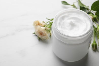 Photo of Jar of hand cream and roses on white marble table, space for text