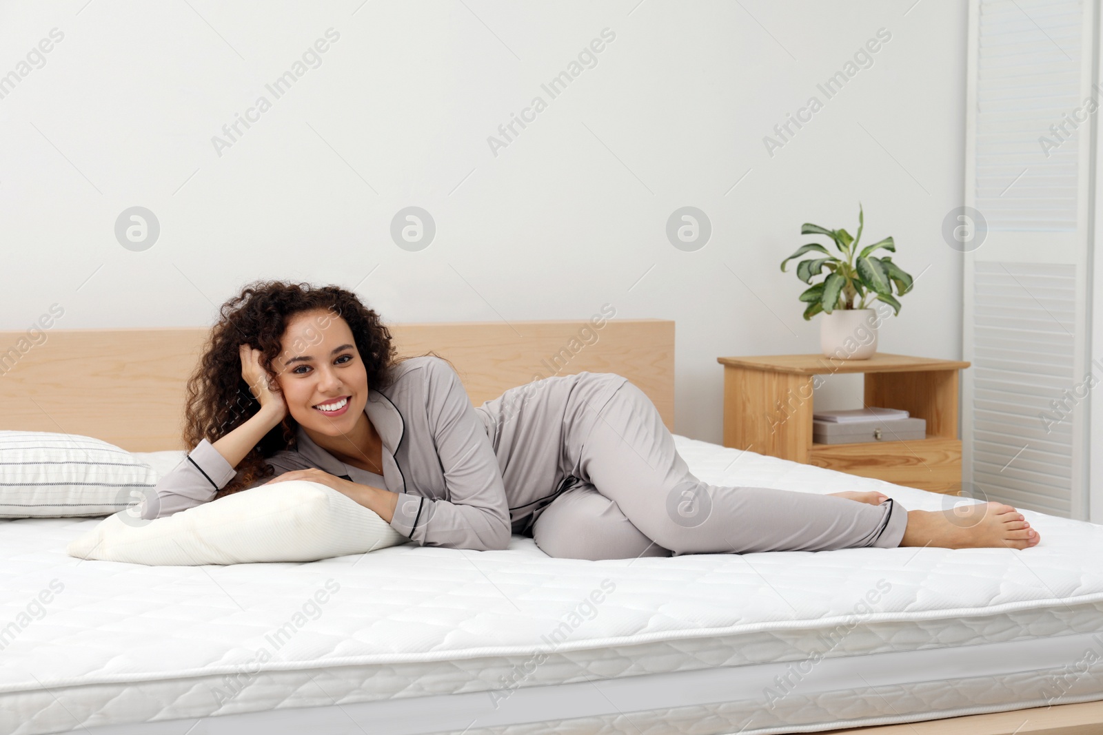 Photo of Happy young African American woman on bed with comfortable mattress and pillow at home