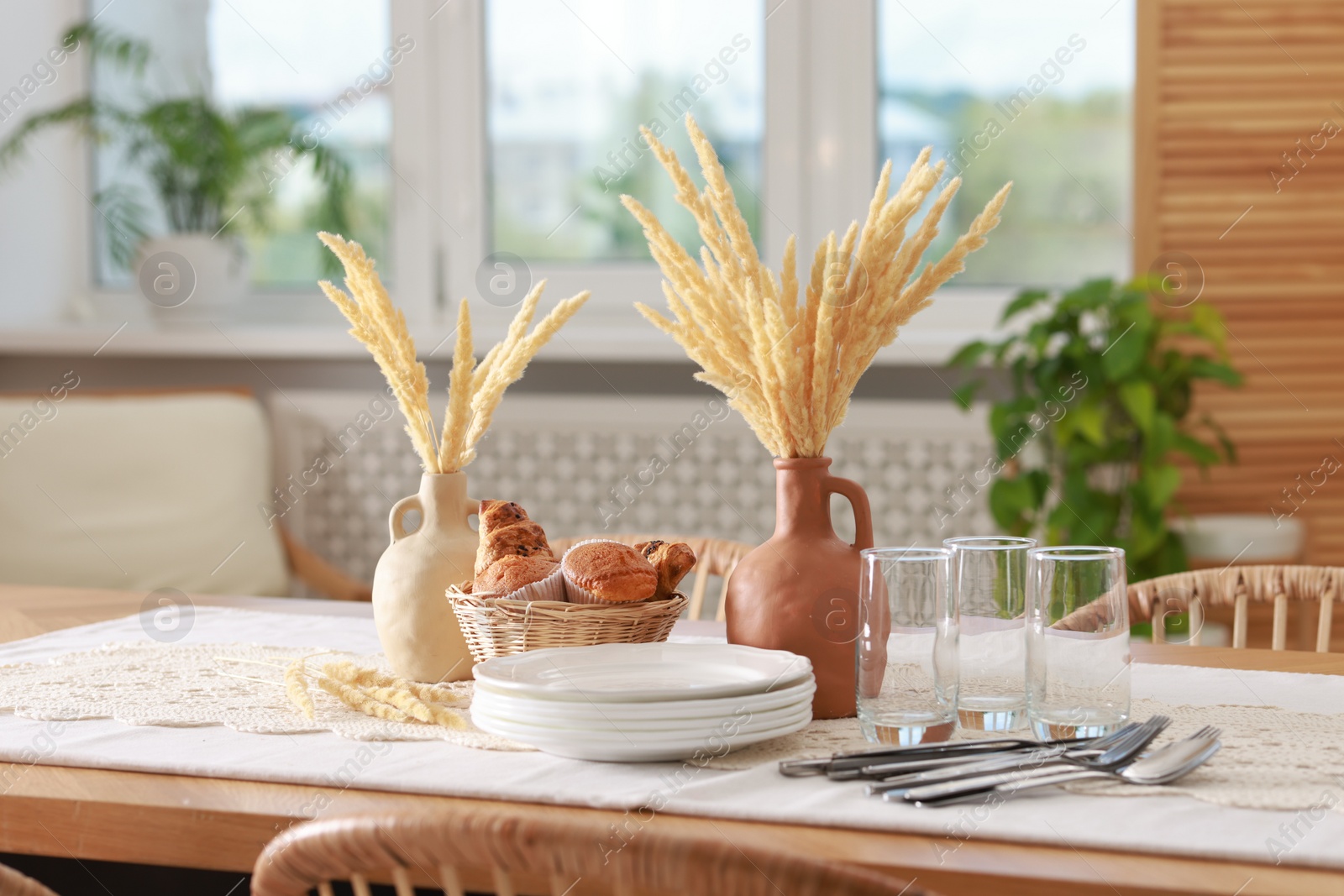 Photo of Clean dishes, dry spikes and fresh pastries on table in stylish dining room