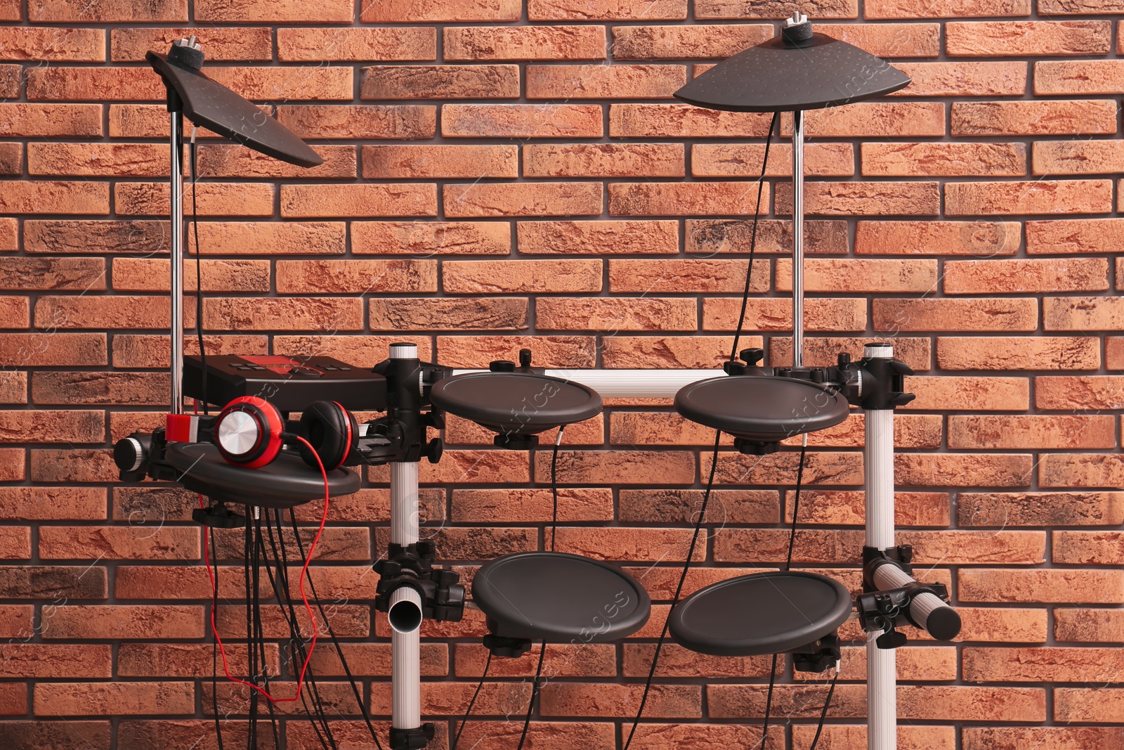 Photo of Modern electronic drum kit near red brick wall indoors. Musical instrument