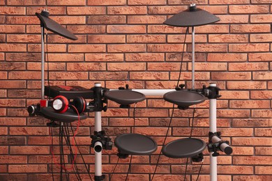 Photo of Modern electronic drum kit near red brick wall indoors. Musical instrument
