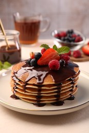 Photo of Stack of tasty pancakes with fresh berries, chocolate sauce and mint on white table, closeup