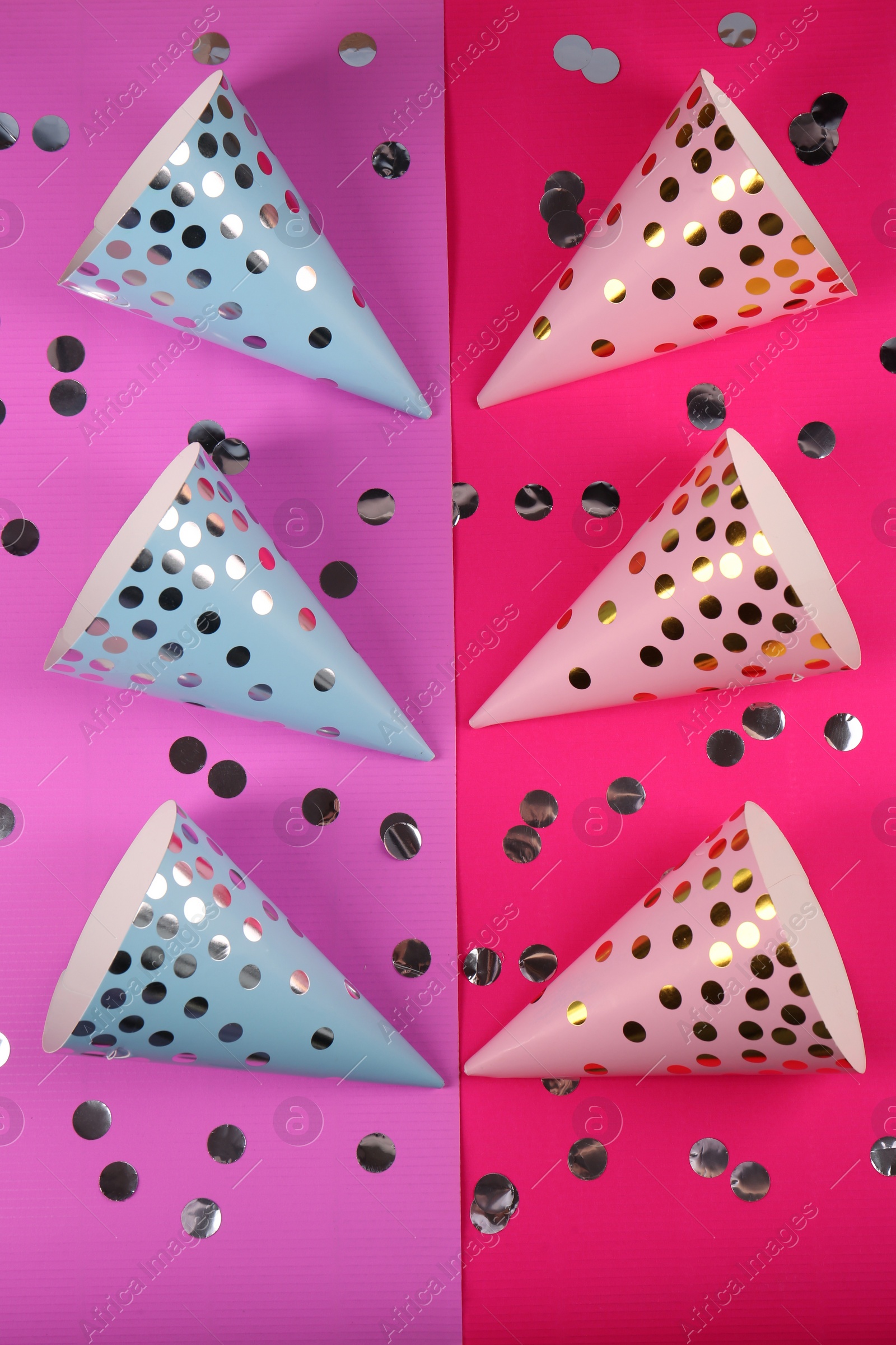 Photo of Bright party hats with confetti on color background, flat lay. Handmade decorations