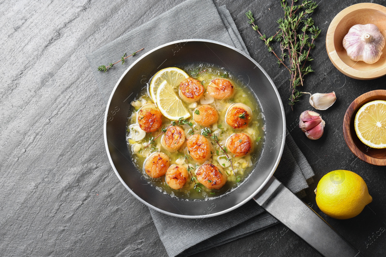 Photo of Delicious scallops with sauce in frying pan and ingredients on dark gray textured table, flat lay