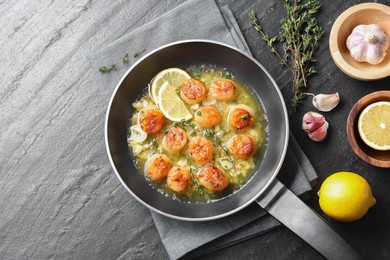 Delicious scallops with sauce in frying pan and ingredients on dark gray textured table, flat lay