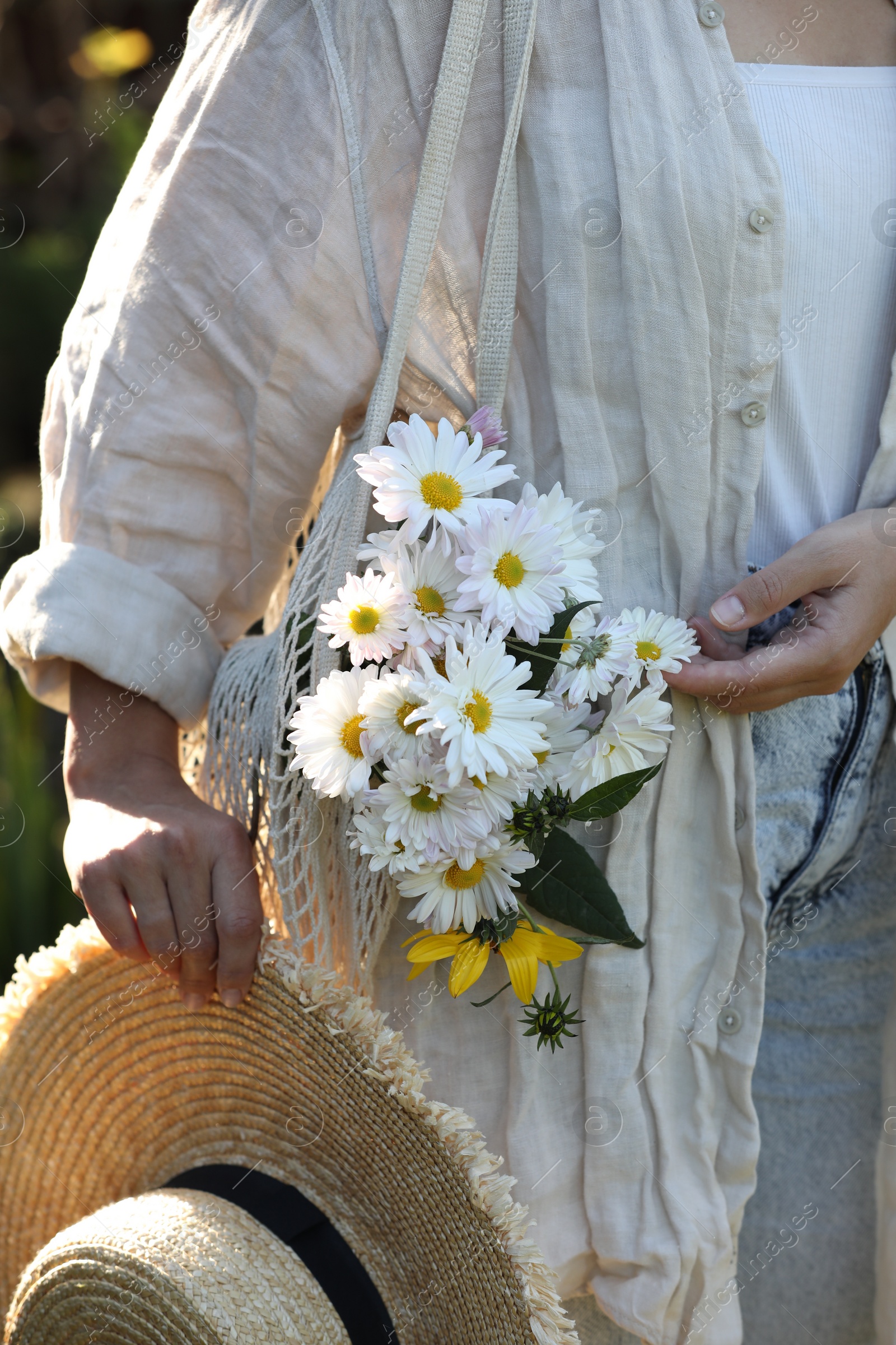 Photo of Woman holding net bag of beautiful white chamomile flowers outdoors, closeup