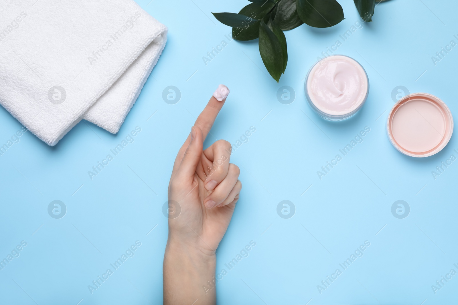 Photo of Woman with jar of body cream on light blue background, top view