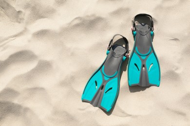 Photo of Pair of turquoise flippers on sand, top view. Space for text