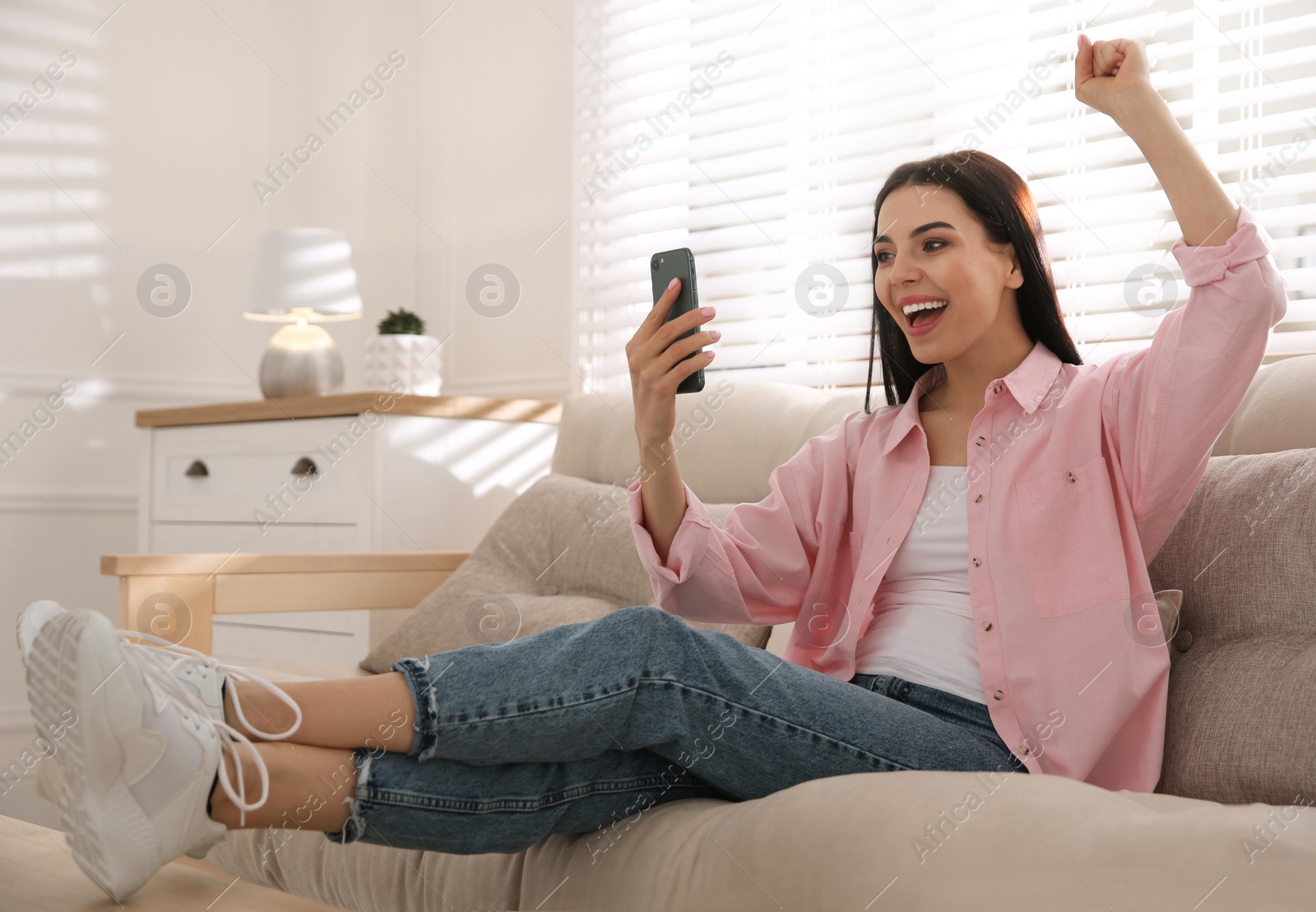 Photo of Emotional woman participating in online auction using smartphone at home