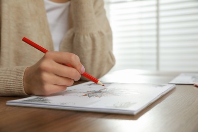 Photo of Young woman coloring antistress page at table indoors, closeup. Space for text