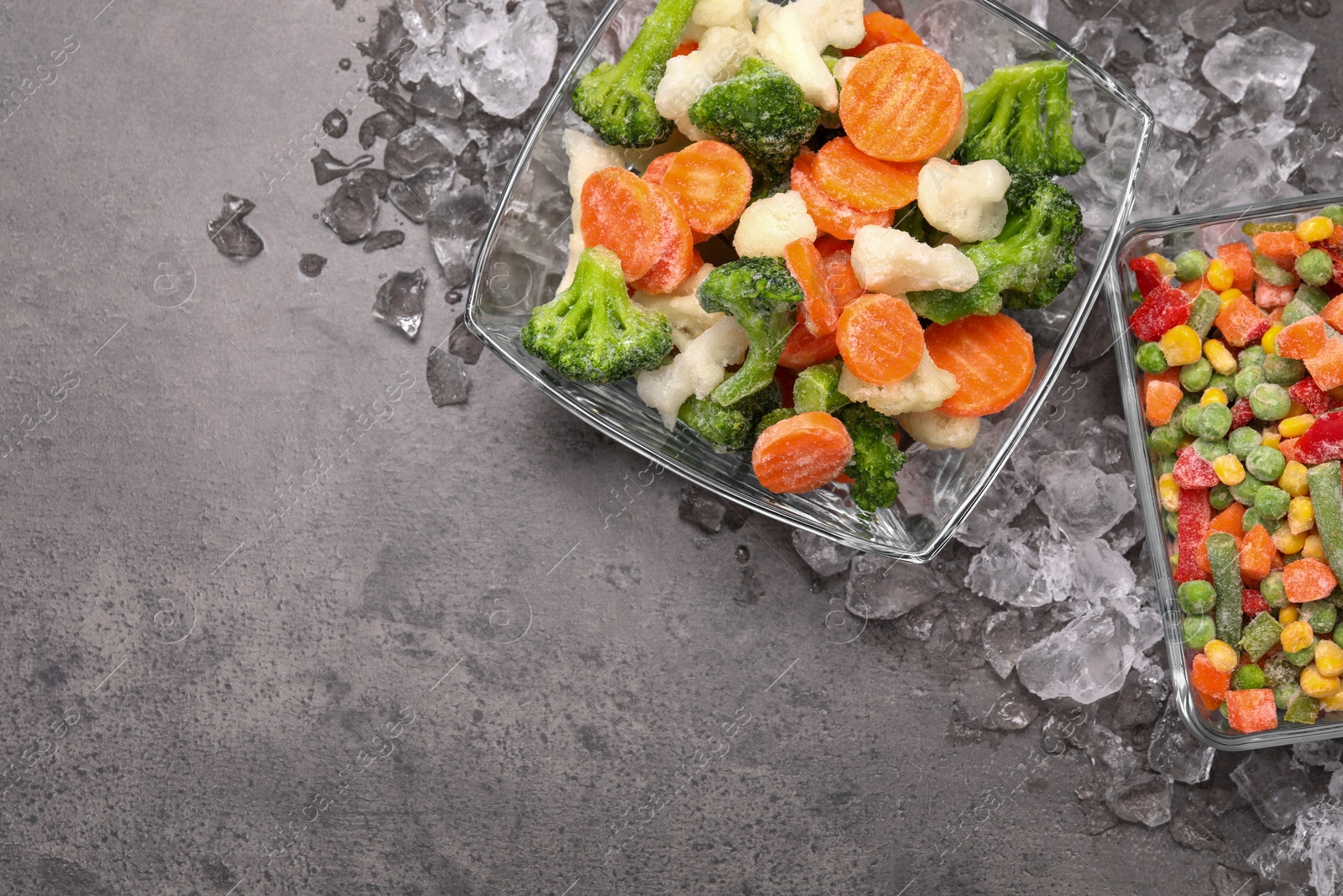 Photo of Mix of different frozen vegetables with ice on grey textured table, flat lay. Space for text