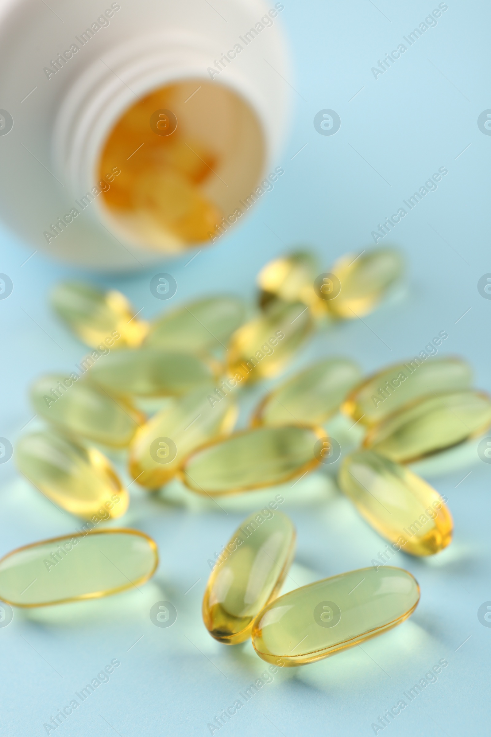 Photo of Bottle and vitamin capsules on light blue background, closeup