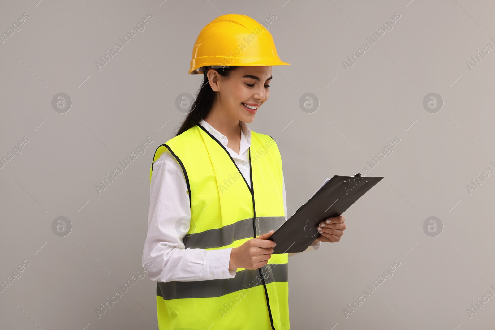 Photo of Engineer in hard hat holding clipboard on grey background