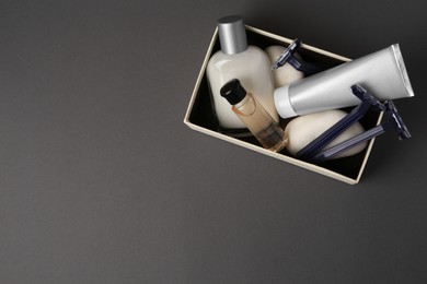 Box with different men's shaving accessories on dark grey background, top view. Space for text
