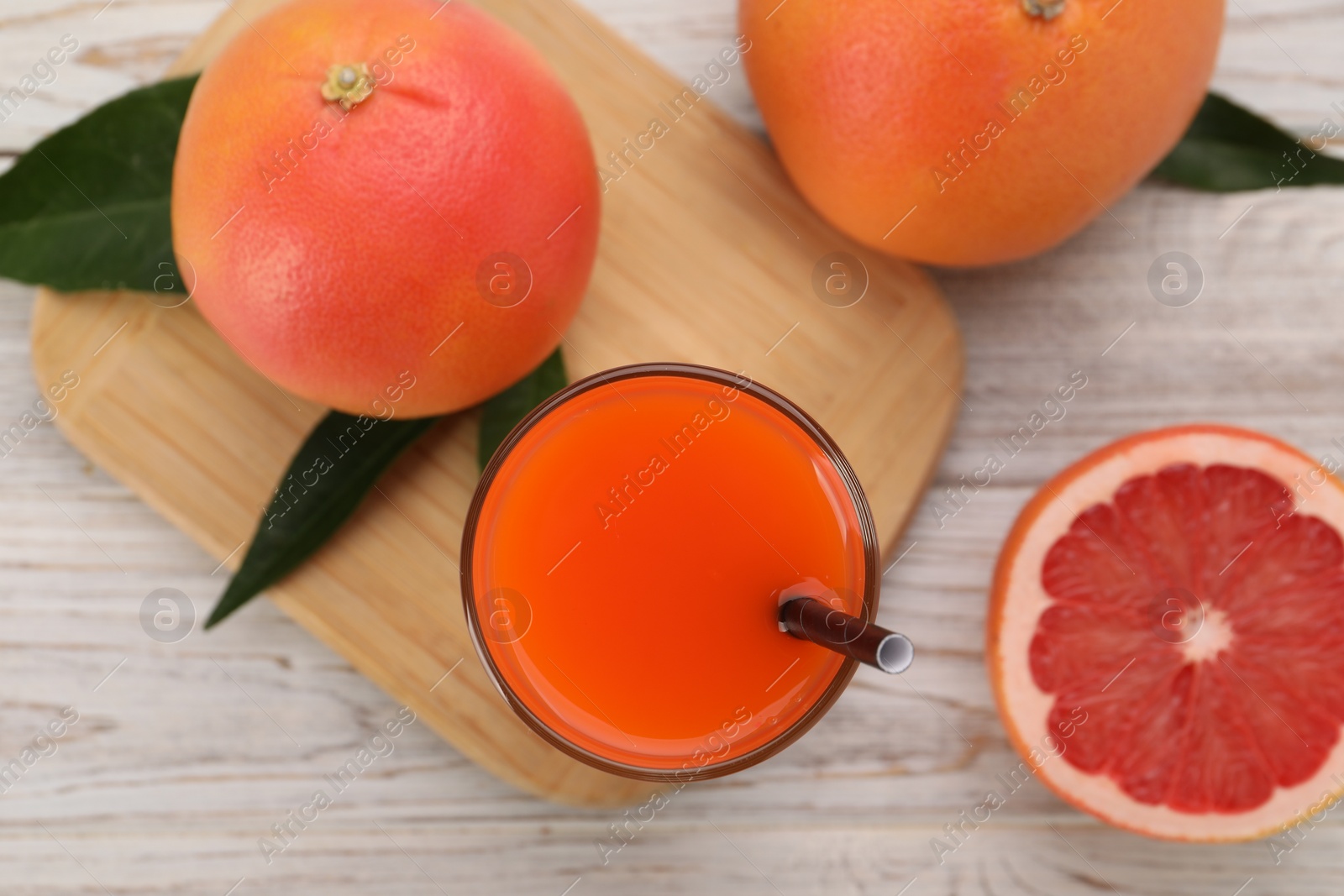 Photo of Tasty grapefruit juice in glass and fresh fruits on light wooden table, flat lay