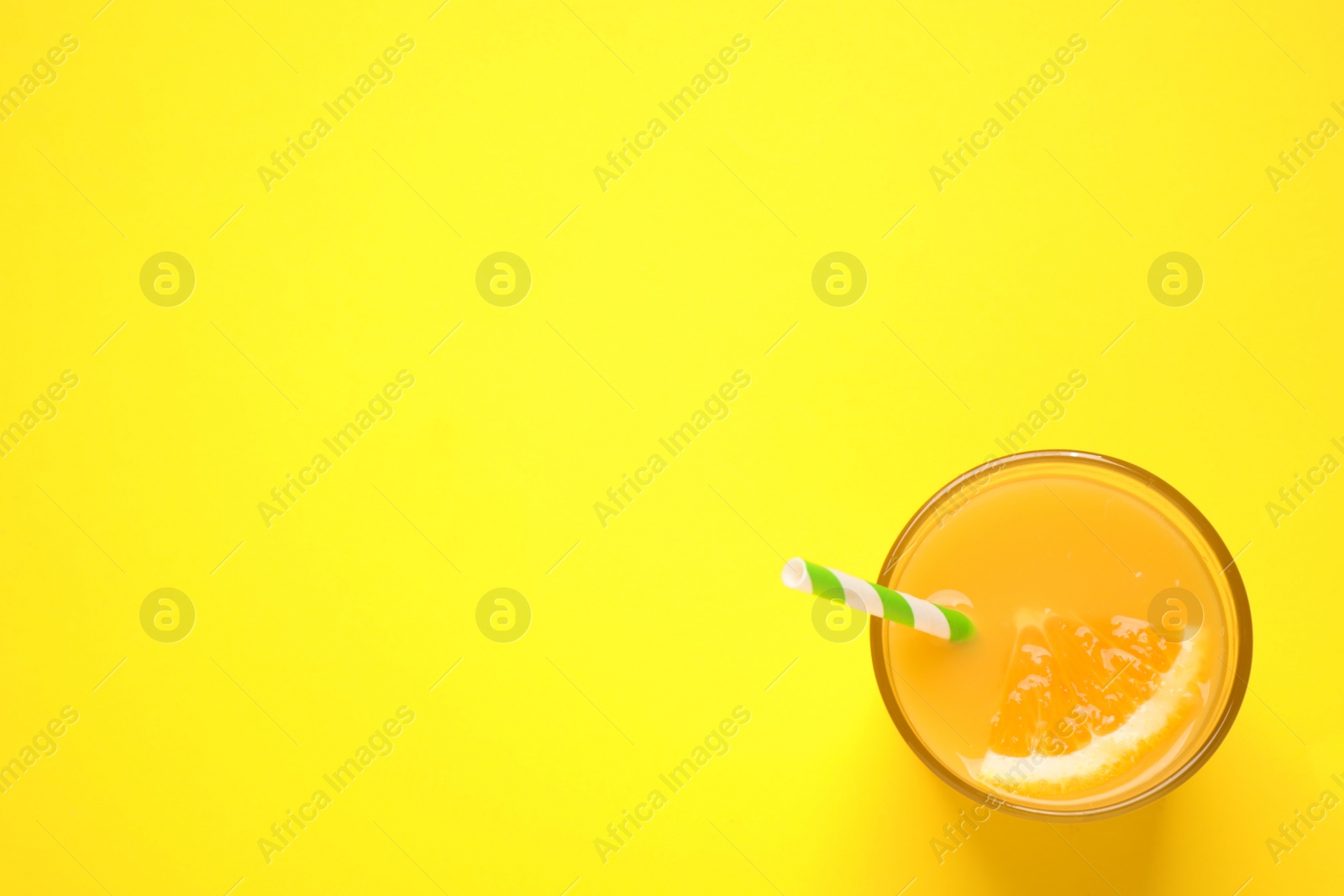 Photo of Glass of orange juice on yellow background, top view. Space for text