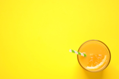 Photo of Glass of orange juice on yellow background, top view. Space for text