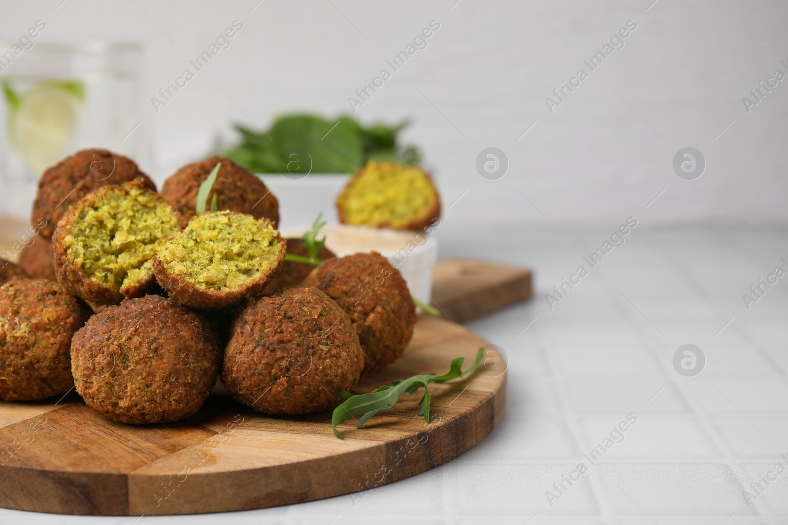 Photo of Delicious falafel balls and arugula on white tiled table, space for text