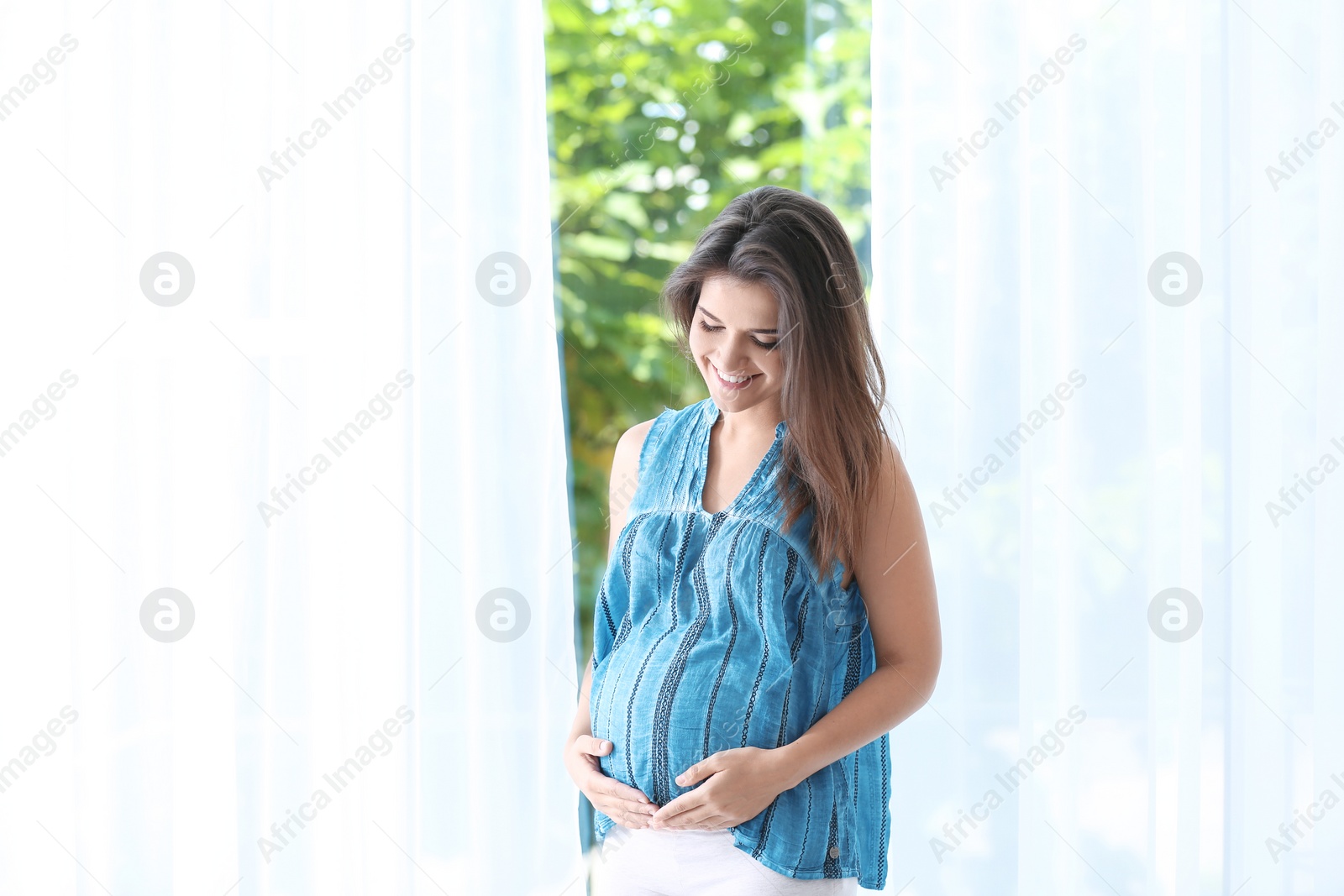 Photo of Happy pregnant woman standing near window at home