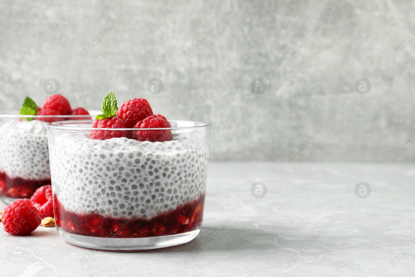 Photo of Delicious chia pudding with raspberries and mint on light marble table, space for text